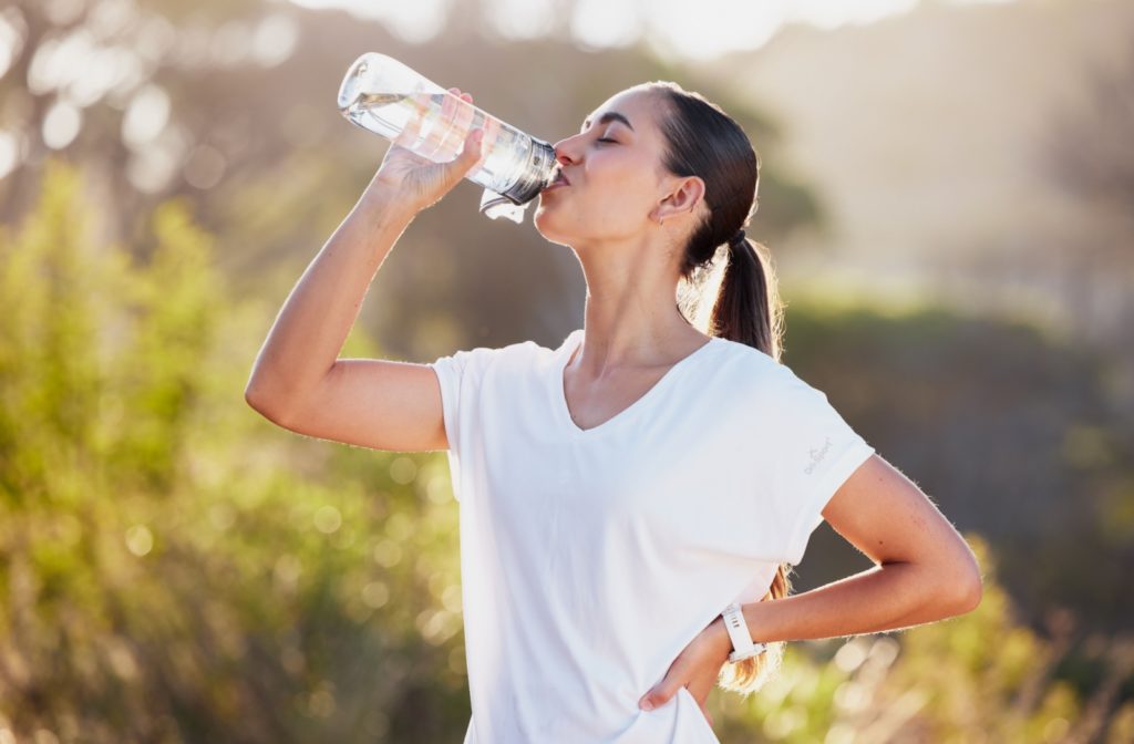 A woman drinking water from her reusable plastic bottle outdoors.
