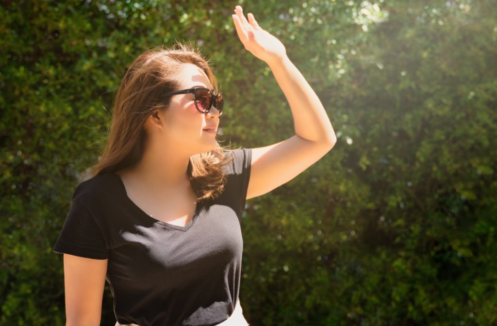 Woman protecting her eyes from the sun with sunglasses and her hand.
