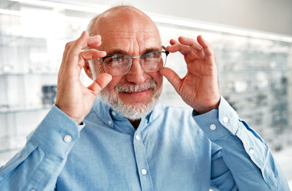 Senior holding up glasses on their face, in an optometry office.