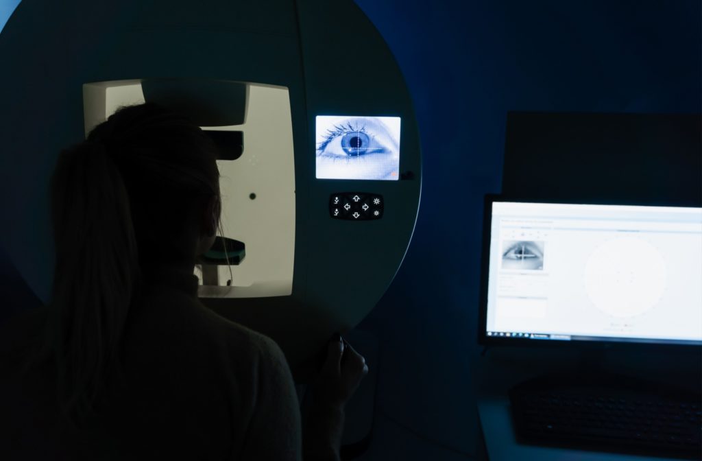 Person taking a visual field test with diagnostic equipment and a computer monitor displaying results.