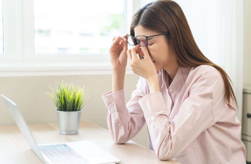 Person sitting at a desk removing their glasses and rubbing their eyes due to discomfort or eye strain