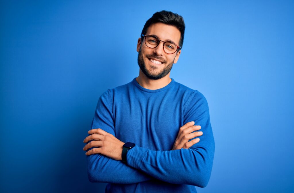 A person with a bright smile and their arms crossed wears Neurolens to address eye misalignment.