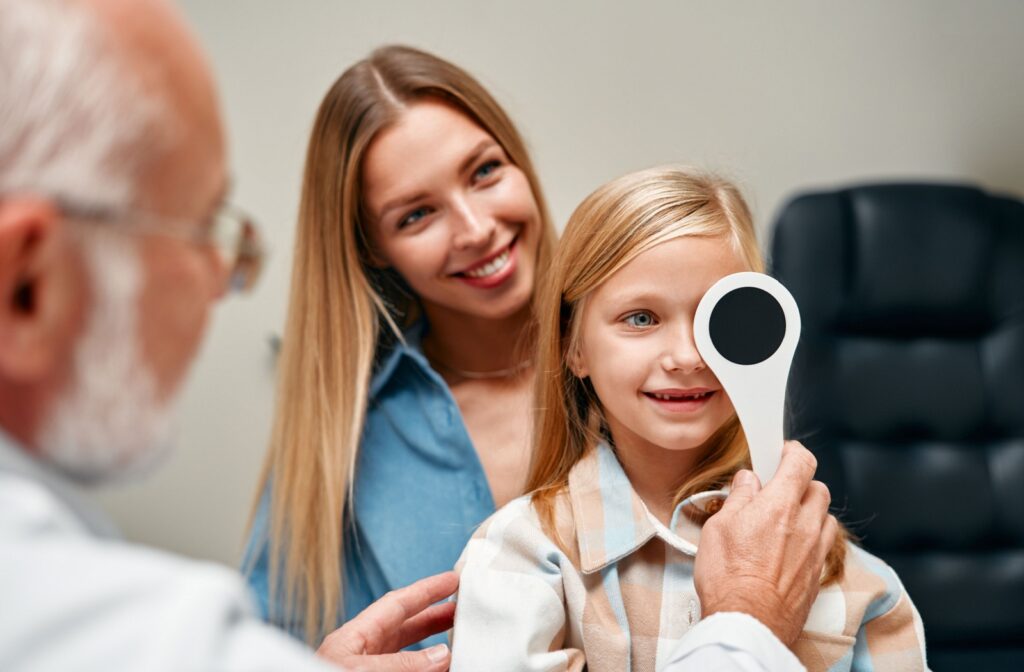 A young girl sitting on her parent's lap at they eye doctor, having her eyes examined to monitor for signs of eye disease.