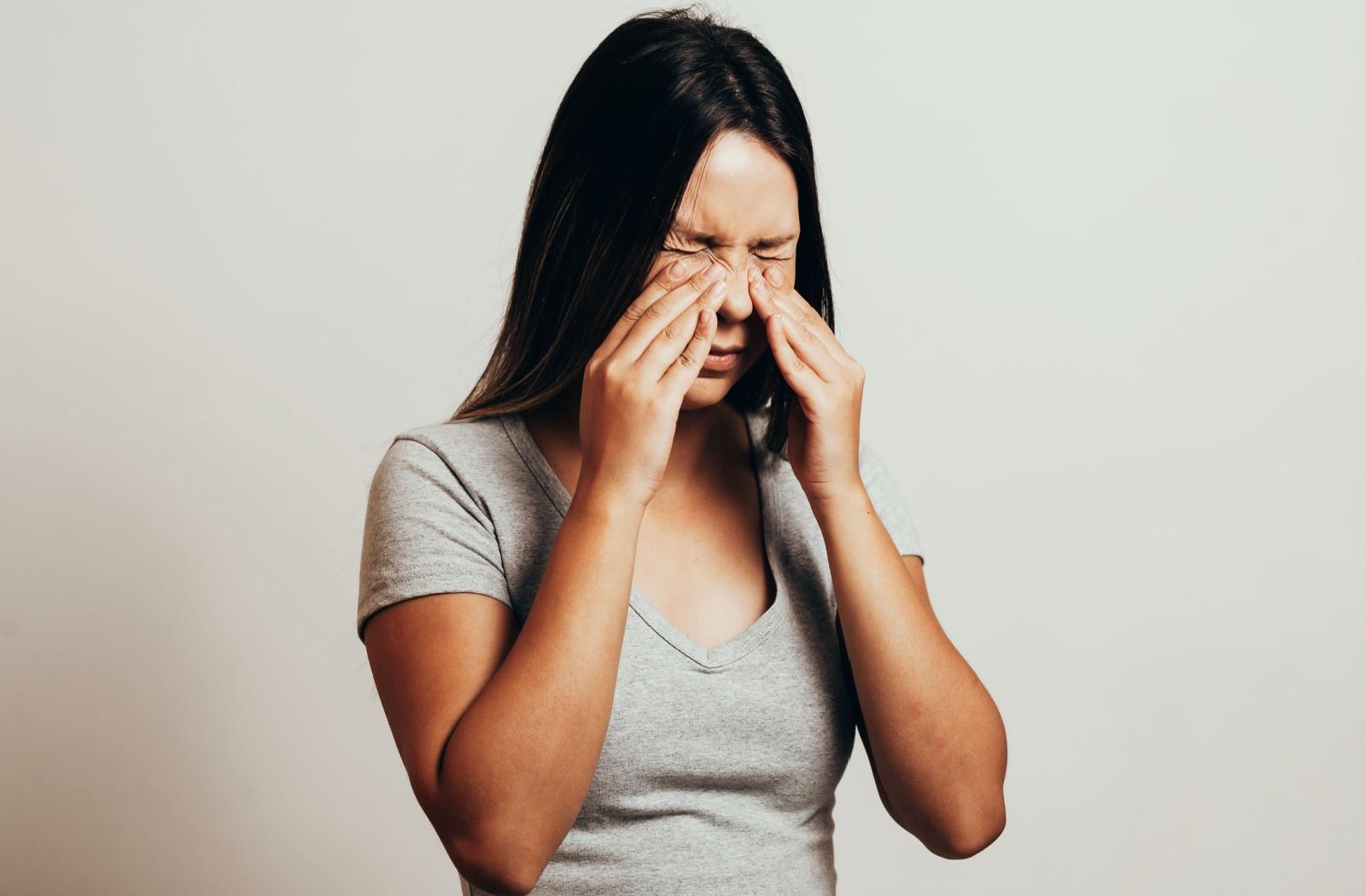 A person pressing their hands on either side of their nose, experiencing pain behind the eye caused by sinus issues.